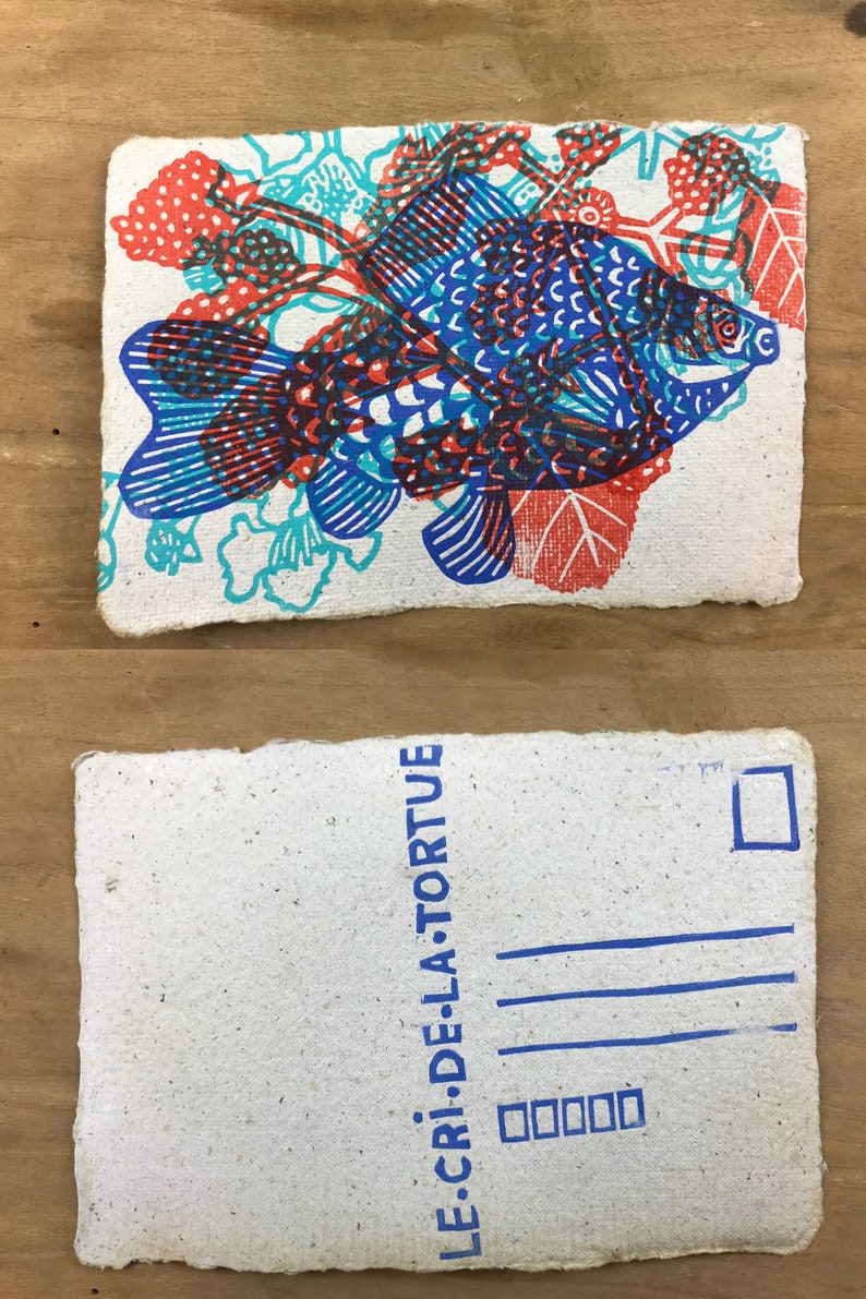 Puede incluir: Una postal blanca con un pez azul y rojo impreso con un dise&ntilde;o. La parte posterior de la postal tiene un sello azul y el texto "LE CRI DE LA TORTUE".