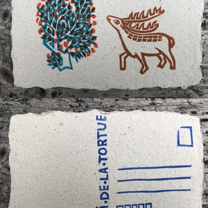 Puede incluir: Una postal con un &aacute;rbol azul y naranja y un ciervo marr&oacute;n en el frente. La parte posterior de la postal tiene el texto "LE CRI DE LA TORTUE" en azul.