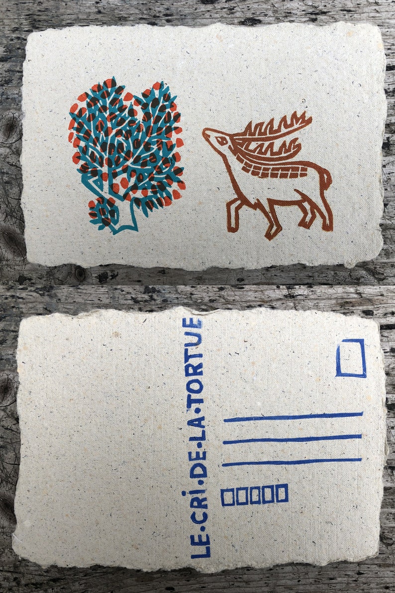 Puede incluir: Una postal con un &aacute;rbol azul y naranja y un ciervo marr&oacute;n en el frente. La parte posterior de la postal tiene el texto "LE CRI DE LA TORTUE" en azul.