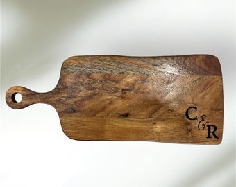 May include: A long, rectangular wooden serving board with a handle. The board has a natural wood grain and is engraved with the initials "C & R".