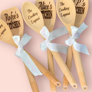 May include: Five wooden spoons with personalised text. The spoons are tied together with white ribbon. The text on the spoons reads "The Cooking Legend", "Rofeee's Kitchen", "Alice's Kitchen", "The Cooking Legend", and "P's Kitchen".
