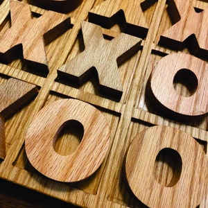 May include: A wooden tic-tac-toe game with the letters X and O cut out of the pieces. The game is made of light brown wood and has a natural finish.