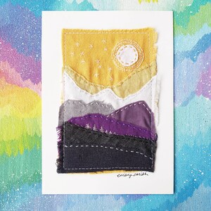 May include: A fabric art piece depicting a mountain landscape with a yellow sky, a white stitched moon, and embroidered stars. The mountains are layered in shades of white, gray, purple, and black. The artist's signature, "emery smith," is in the bottom right corner.