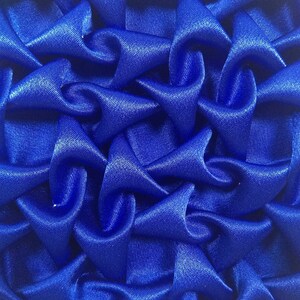 May include: A close-up of a blue fabric with a textured, quilted pattern. The fabric is made of a soft, silky material and has a slightly shiny finish.