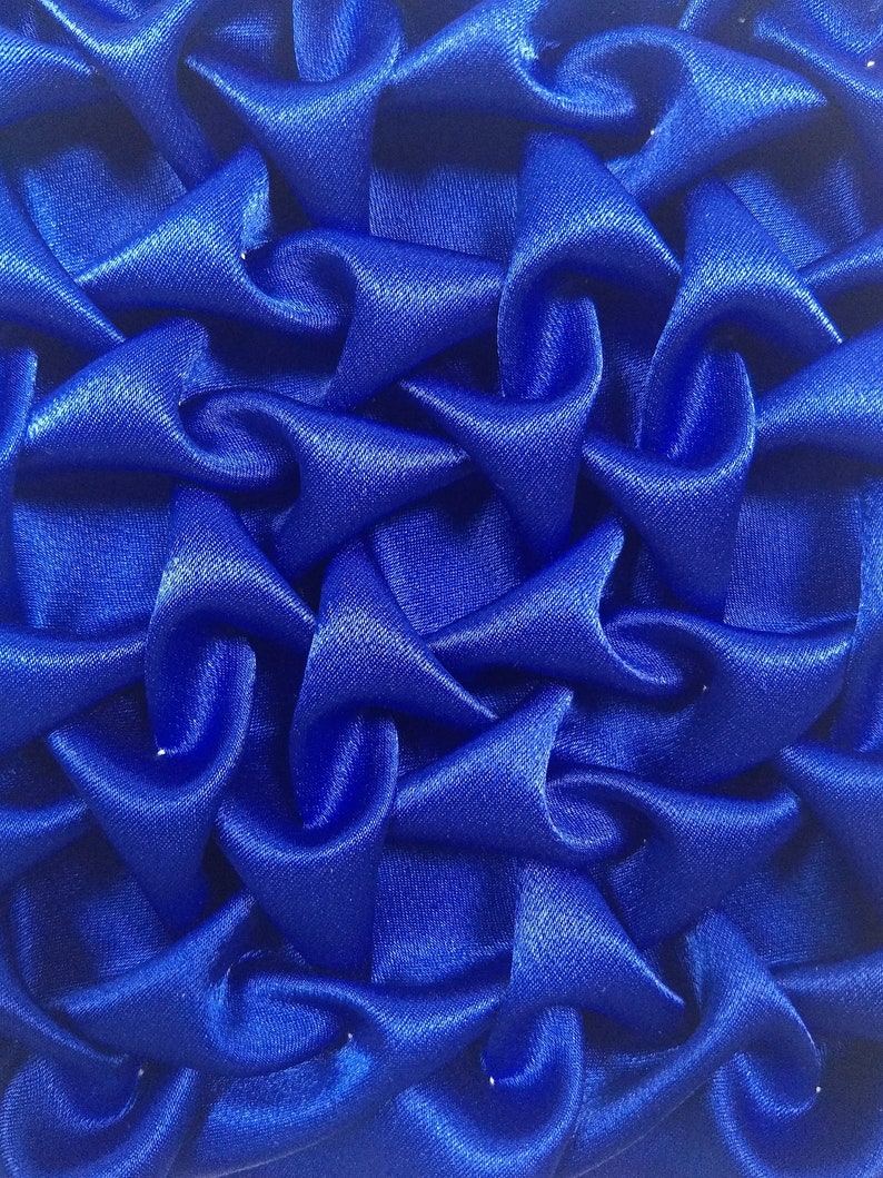 May include: A close-up of a blue fabric with a textured, quilted pattern. The fabric is made of a soft, silky material and has a slightly shiny finish.