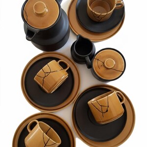 Könnte beinhalten: Ein Keramik-Teeservice in Schwarz und Beige. Das Set umfasst eine Teekanne, Tassen, Untertassen, einen Sahnekännchen und eine Zuckerdose. Die Tassen und die Teekanne haben ein einzigartiges Craquelé-Design.
