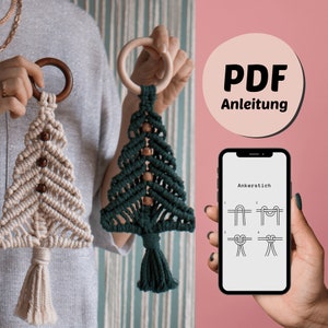 Könnte beinhalten: Zwei Makramee-Weihnachtsbaum-Anhänger, einer in Beige und einer in Grün, mit Holzperlen und Quasten. Ein Smartphone zeigt eine PDF-Anleitung zum Herstellen der Anhänger, mit dem Text "PDF Anleitung" und "Ankerstich" sichtbar.