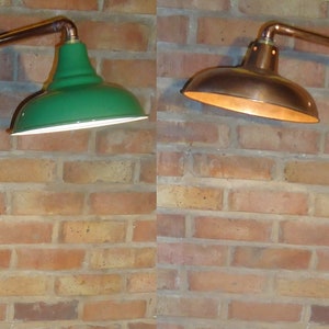 May include: A copper floor lamp with a green and a copper shade. The lamp is made of copper pipe and has a square base. The lamp is standing on a wooden floor in front of a brick wall.