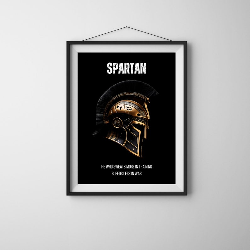 May include: Framed art print featuring a Spartan helmet design. The helmet is gold and black, with the word "SPARTAN" at the top and the quote "HE WHO SWEATS MORE IN TRAINING BLEEDS LESS IN WAR" at the bottom. The background is black.