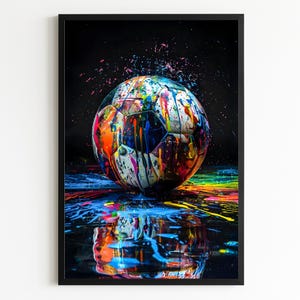 May include: A framed art print featuring a football covered in vibrant paint splatters. The ball is white with black panels, and the paint is a mix of blue, orange, yellow, and pink. The artwork is reflected in a dark, glossy surface.