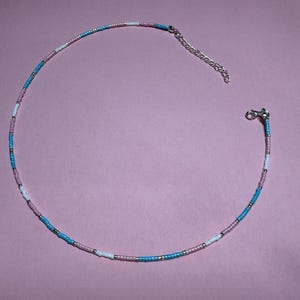 May include: A delicate beaded necklace with a colour block design. The necklace alternates between light blue, white, and pink beads, with silver-toned metal accents and a clasp. The necklace is approximately 40 cm long.