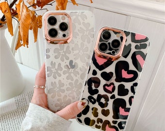 Op de afbeelding: Twee transparante telefoonhoesjes met bloemen- en luipaardprints. De ene hoes heeft een wit bloemenpatroon, de andere een zwart, roze en grijze luipaardprint. Beide hoesjes hebben een roségouden cameralensbeschermer.