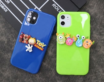 Op de afbeelding: Twee telefoonhoesjes: één blauw, één groen. De blauwe hoes heeft een Coca-Cola fles, een tijger, een kat en een witte handschoen, met de tekst "Toy Story". De groene hoes heeft kleurrijke monsterachtige figuren.