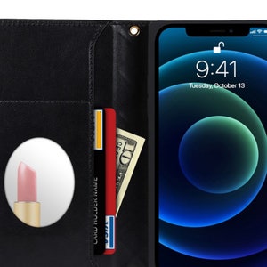 Puede incluir: Funda de tel&eacute;fono de cuero negro con un marco dorado, que contiene un tel&eacute;fono inteligente que muestra la hora y la fecha. La funda tiene ranuras para tarjetas, un espejo y un billete de diez d&oacute;lares. Tambi&eacute;n se ve un l&aacute;piz labial rojo y un l&aacute;piz labial rosa.