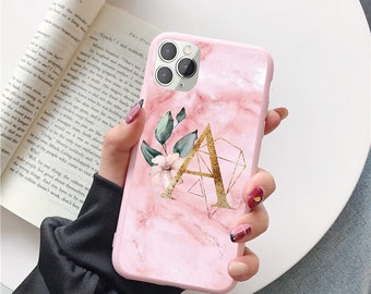 Op de afbeelding: Roze marmerpatroon telefoonhoesje met een gouden geometrische letter "A" en bloemaccenten. De hoes heeft een zachte roze rand en een glanzende afwerking, wat zorgt voor een stijlvol en beschermend ontwerp voor een smartphone.