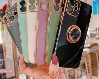 Op de afbeelding: Een hand houdt een waaier van kleurrijke telefoonhoesjes vast. De hoesjes zijn in tinten groen, wit, paars en zwart, met goudkleurige randen en cameraringen. Elke hoes heeft een metalen ringhouder aan de achterkant. De merknaam "caseolux" is zichtbaar.