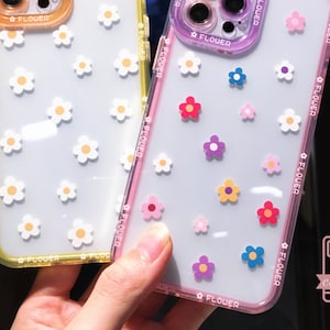 Puede incluir: Fundas transparentes para teléfono con diseños florales coloridos. Una funda tiene un borde amarillo, la otra un borde rosa. Las fundas están decoradas con flores blancas, rosas, rojas, azules y moradas. La palabra "FLOWER" está impresa en los bordes.