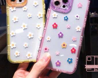 Op de afbeelding: Transparante telefoonhoesjes met kleurrijke bloemmotieven. Eén hoesje heeft een gele rand, de andere een roze rand. De hoesjes zijn versierd met witte, roze, rode, blauwe en paarse bloemen. Het woord "FLOWER" staat op de randen.
