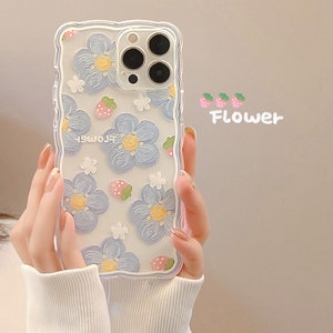 May include: Clear phone case with a wavy edge, featuring a pattern of blue flowers, strawberries, and small white flowers. The word "Flower" is written in pink script. The case is held in front of a light background.