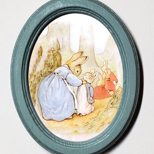 May include: A framed illustration of a blue-dressed rabbit with a white apron, helping a smaller rabbit put on a jacket. Other rabbits are in the background.