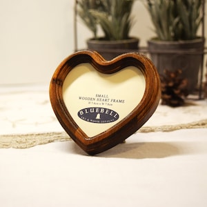 May include: A small wooden heart-shaped picture frame with a brown finish. The frame measures 7.4cm x 7.8cm and has the text "SMALL WOODEN HEART FRAME" and "BLUEBELL ART & WOOD DESIGNS" printed on it.