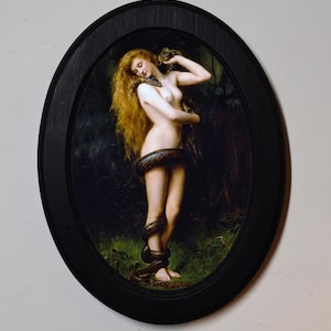 Pode incluir: Uma impressão emoldurada oval de uma pintura clássica. A obra de arte retrata uma figura nua com longos cabelos ruivos, enroscada por uma cobra. A pintura é ambientada em um fundo escuro e florestal. A moldura é preta.