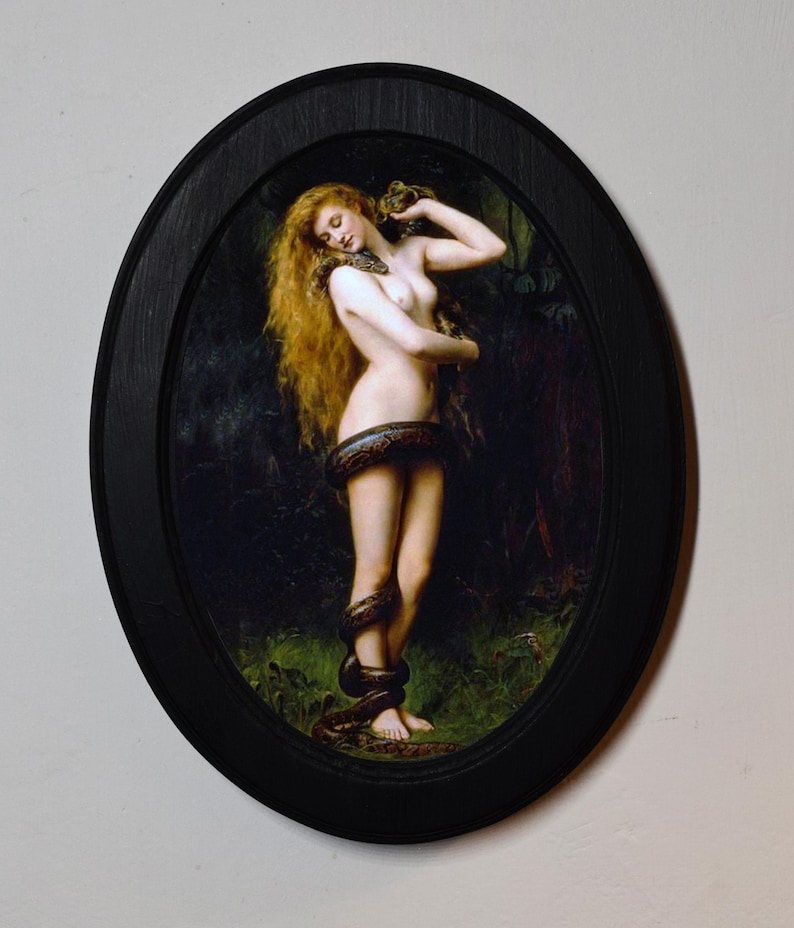 May include: An oval framed print of a classical painting. The artwork depicts a nude figure with long red hair, entwined by a snake. The painting is set against a dark, forested background. The frame is black.