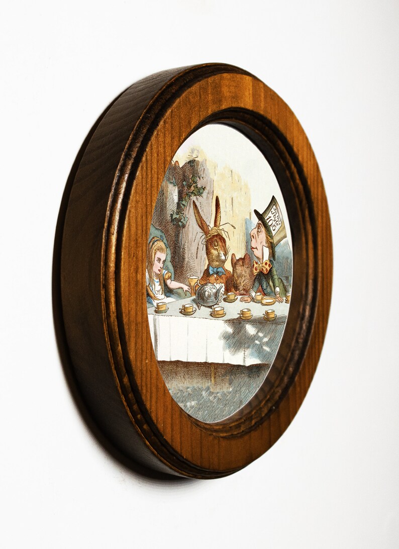 May include: A framed illustration of a tea party scene from Alice's Adventures in Wonderland. The Mad Hatter, the March Hare, and Alice are seated at a table with a teapot and cups. The illustration is in a brown oval frame.