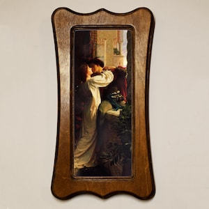 May include: A framed print featuring a romantic scene of a couple embracing. The artwork depicts a man and woman in period clothing, set against an outdoor backdrop. The frame is made of wood with a decorative, scalloped edge.
