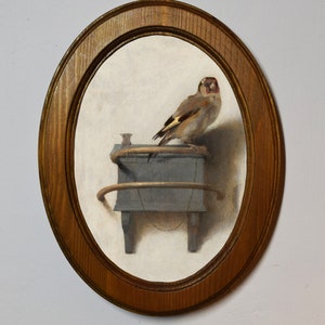 May include: A framed painting of a small bird perched on a wooden shelf with a small decorative object. The bird is brown and white with a red head and a yellow beak. The shelf is painted a dark blue color.