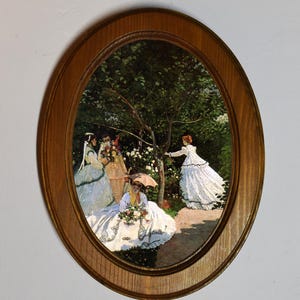 May include: An oval framed print of a painting depicting four women in white dresses in a garden setting. The women are surrounded by green trees and white flowers. The painting is in a wooden frame.