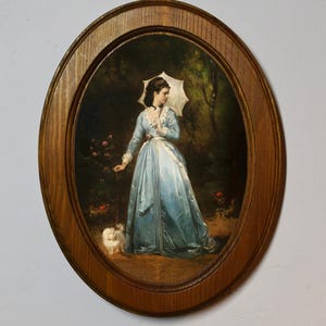 以下が含まれることがあります： 青いドレスを着た女性が日傘を持ち、小さな白い犬と散歩している楕円形の額入り絵画。 木のフレームの中に、木や花のある庭が描かれています。