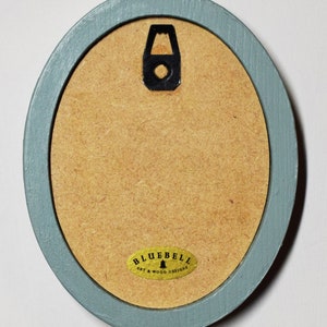 May include: A light blue oval picture frame with a gold label that reads "Bluebell Art & Wood Designs".