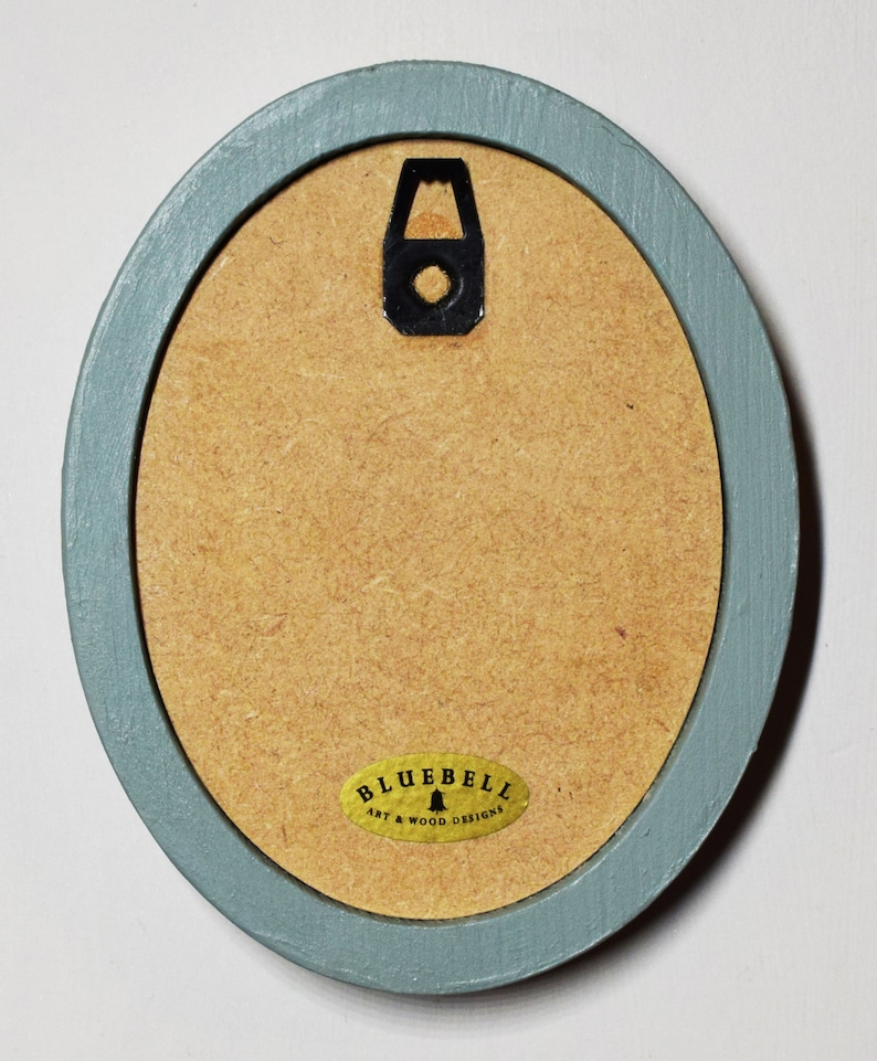 May include: A light blue oval picture frame with a gold label that reads "Bluebell Art & Wood Designs".