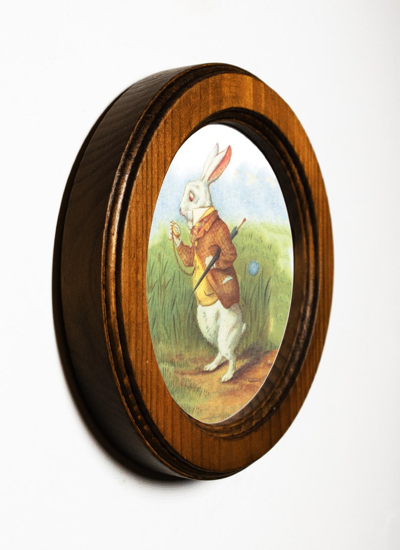 May include: A framed illustration of a white rabbit wearing a waistcoat and holding a pocket watch. The rabbit is standing in a grassy field with a blue flower.