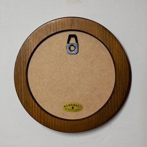May include: A round wooden picture frame with a brown finish. The frame has a metal hanger on the back. The frame is empty and ready for a picture.