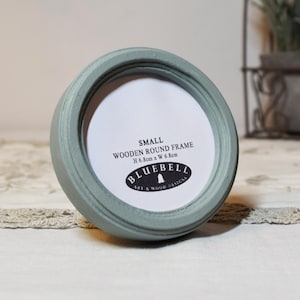 May include: A small, round, light blue wooden picture frame with a white mat. The frame measures 6.8cm x 6.8cm and has the text "SMALL WOODEN ROUND FRAME" and "BLUEBELL ART & WOOD DESIGNS" printed on it.
