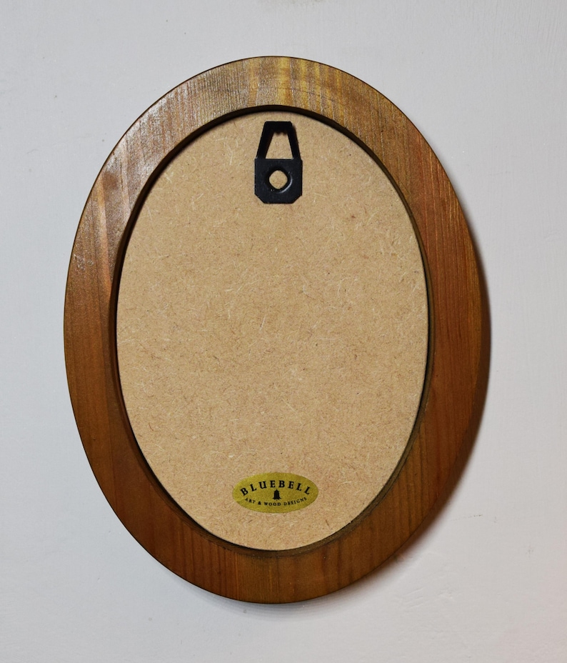 Pu&ograve; includere: Cornice ovale in legno con finitura marrone. La cornice ha un gancio per appendere sul retro e un adesivo dorato con il testo "Bluebell Art & Wood Designs".