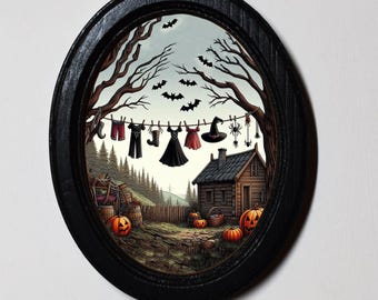 May include: Oval framed artwork with a Halloween theme. A clothesline displays miniature garments, a witch hat, and spiders. A rustic cabin sits in a spooky landscape with pumpkins and bats. The frame is black.