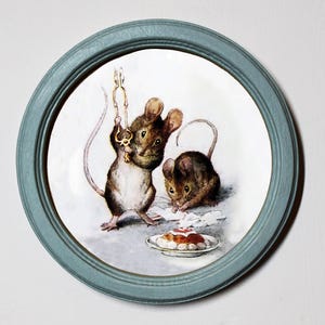 May include: A round ceramic plate with a blue frame depicts two mice. One mouse is holding a key and the other is eating a pastry. The plate has a white background.