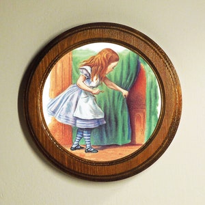 May include: A framed illustration of a young girl in a blue and white dress, with long red hair, looking through a small door. The door is behind a green curtain.