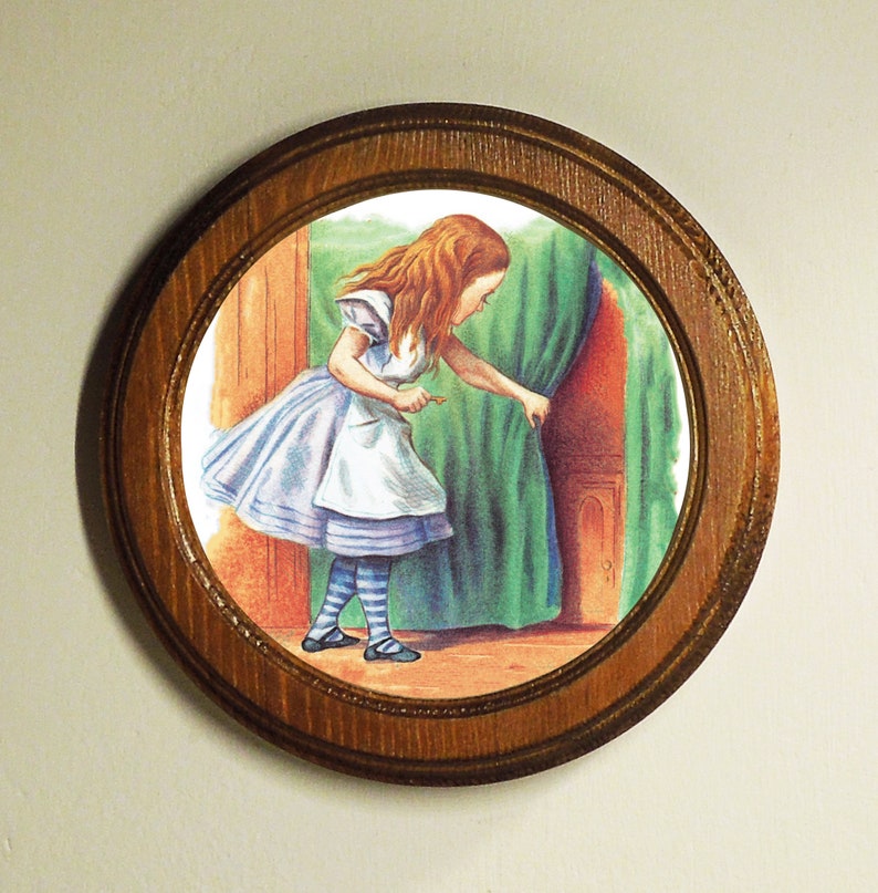 May include: A framed illustration of a young girl in a blue and white dress, with long red hair, looking through a small door. The door is behind a green curtain.