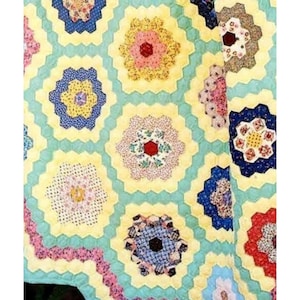 May include: A quilt made from colourful fabric scraps in a hexagonal pattern. The quilt is made up of many different colours, including red, blue, yellow, green, and pink. The quilt is a traditional style and is a beautiful example of patchwork.