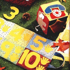 May include: A colourful, handmade educational toy set featuring a fabric number strip with numbers 3-10, hand cutouts, and a telephone-shaped block. The numbers and hand cutouts are yellow, and the block has a red, yellow, and blue design.
