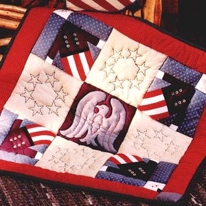 May include: A patriotic quilt with a red border and a patchwork design. The quilt features squares with stars, stripes, and an eagle motif in red, white, and blue. The quilt is likely handmade and evokes a sense of Americana.