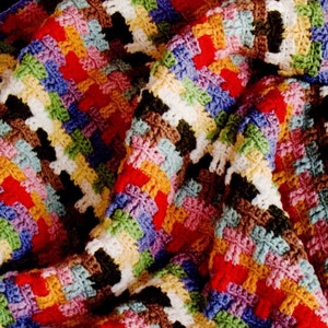 Puede incluir: Una manta de ganchillo hecha a mano con un diseño de patchwork colorido. La manta muestra una variedad de colores, incluyendo rojo, azul, verde, amarillo y blanco, dispuestos en un patrón de rayas. La textura de las puntadas de ganchillo es visible.