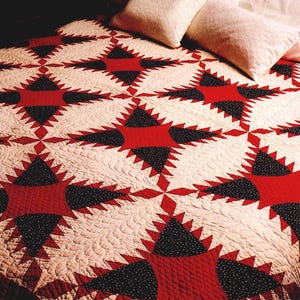 May include: A handmade quilt featuring a repeating starburst pattern in red, black, and cream. The quilt has a detailed, quilted texture and is likely made of cotton. The design is symmetrical and geometric, suitable for a bedspread.