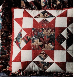 Może przedstawiać: Poduszka w patchworku w kolorze czerwonym, białym i zielonym z wzorem gwiazdy. Poduszka jest otoczona falbanką.