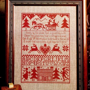 May include: A framed cross-stitch sampler on light tan linen featuring red thread embroidery. The design includes a horse-drawn sleigh, reindeer, a heart, pine trees, and a cottage. It displays the alphabet and the poem: I knew by the smoke, that so gracefully curled Above the green elms, that a cottage was near, And I said, If there's peace to be found in the world, A heart that was humble might hope for it here! T. Moore.