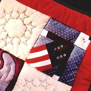 May include: Close-up of a quilted patchwork with patriotic themes. The quilt features red and white stripes, blue polka dots, and a white star pattern. An embroidered eagle is also visible. The quilt is bordered with a red fabric.
